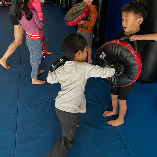 kids punching hand mat while practicing mixed martial arts at Elite Training Center
